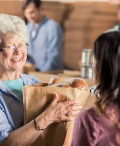 smiling senior woman being handed bag of food by volunteer